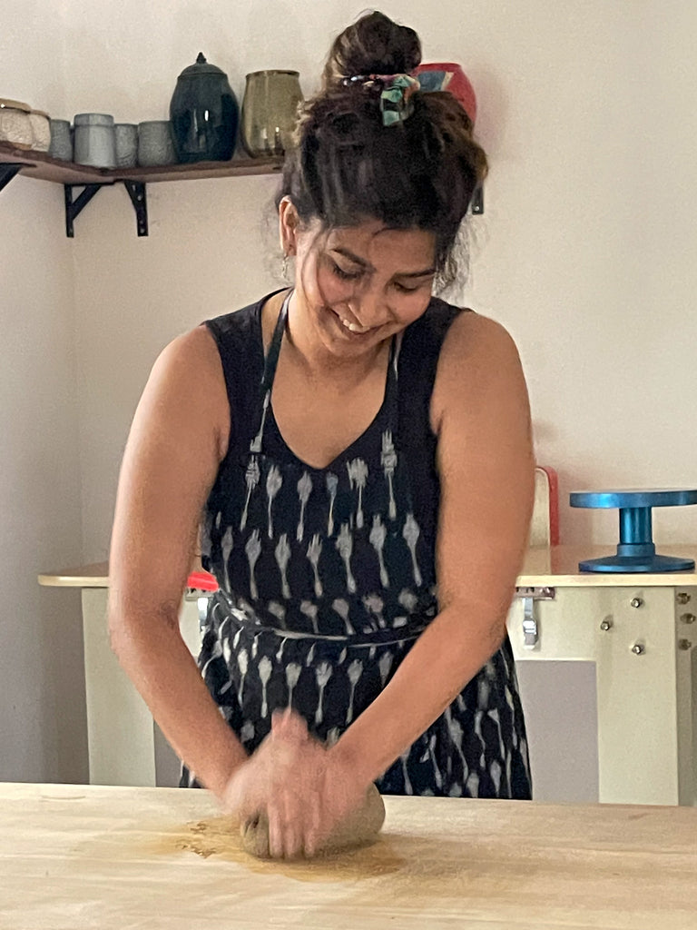 Artist portrait of Gauri Oak wedging clay on a wedging table in her ceramics studio